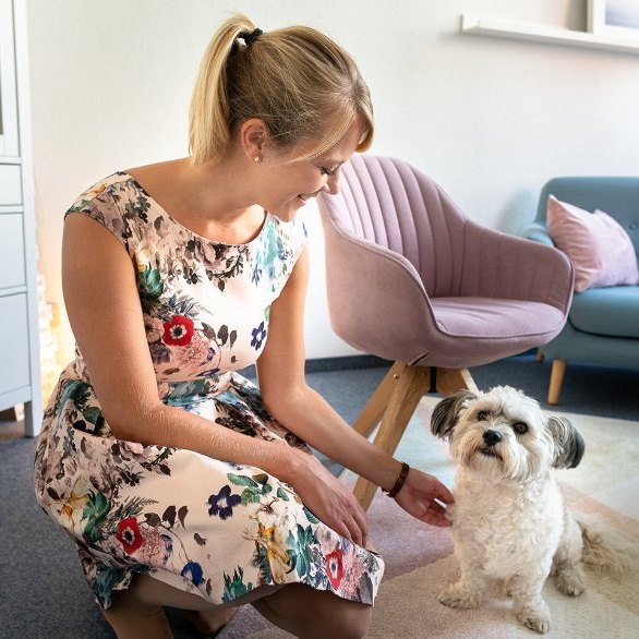 Hanna Berlage kniet in ihrer Praxis neben einem kleinen weißen Hund